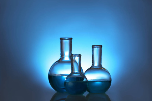 Laborgläser mit Flüssigkeit auf farbigem Hintergrund. Lösungschemie - Foto, Bild