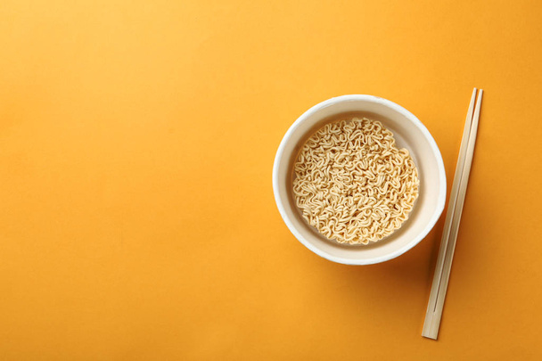 Cup of instant noodles with chopsticks on color background, top view. Space for text - Fotoğraf, Görsel