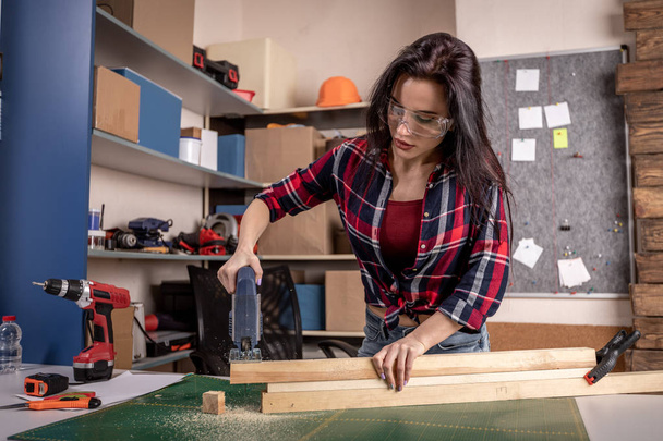 Inicio bricolaje mujer tablón de corte de madera en el banco de trabajo con sierra renovar mejorar y decorar el hogar
 - Foto, Imagen