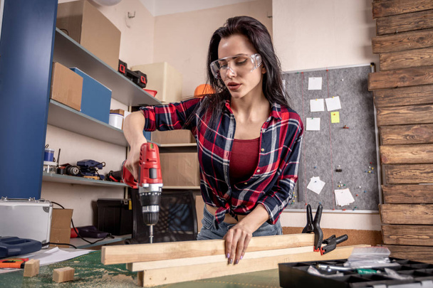 Mujer montando muebles nuevos en el taller en una camisa roja y gafas
 - Foto, imagen