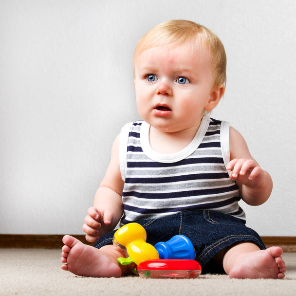 Young toddler sitting up on the floor with a ring and a toy hammer to play with. - Foto, Bild