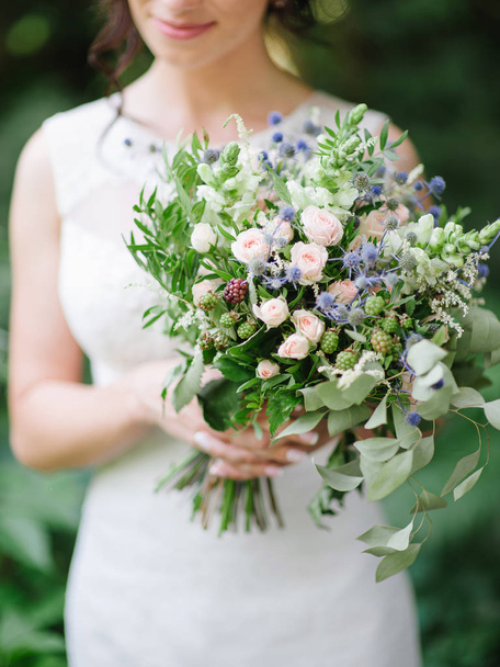Esküvői szertartás. Fiatal menyasszony tartja túlméretezett esküvői csokor kék bogáncs virágok, jana rózsák, eukaliptusz levelek közelről. - Fotó, kép
