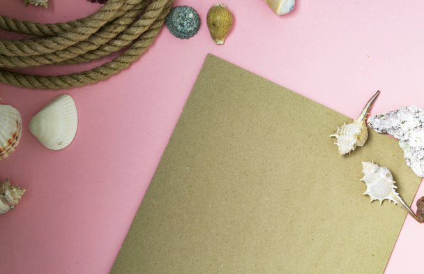 Summertime marine vacation background with lots of seashells, pebbles, nautical rope on pink background. There is a sheet of paper for text, congratulations, inscriptions. - 写真・画像