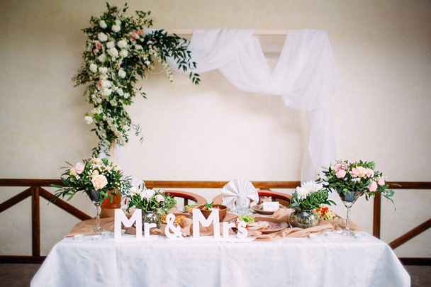 Rusztikus esküvő. Mr. és Mrs. Étterem belső díszített esküvői ünnepség, friss házasok asztala íves és természetes virágok, fehér asztalterítő. - Fotó, kép
