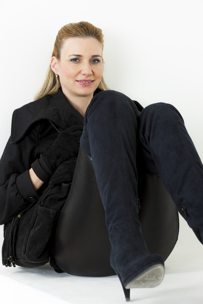 Mulher sentada vestindo roupas pretas e botas com uma bolsa
 - Foto, Imagem