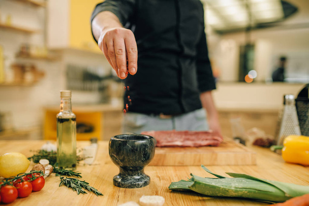 Férfi személy pácolás nyers húst a fából készült hajón, konyha belső háttérben. Chef főzés szűzpecsételbe zöldség, fűszerek és fűszernövények - Fotó, kép