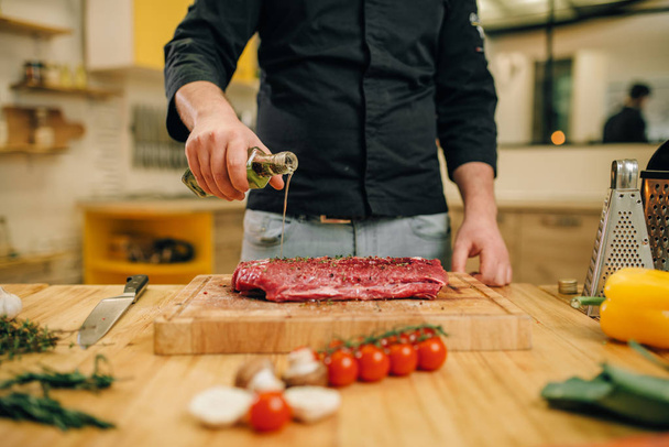 Férfi személy kezek fűszerezés darab nyers húst fa fedélzeten, konyha belső háttérben. Chef főzés szűzpecsételbe zöldség, fűszerek és fűszernövények - Fotó, kép