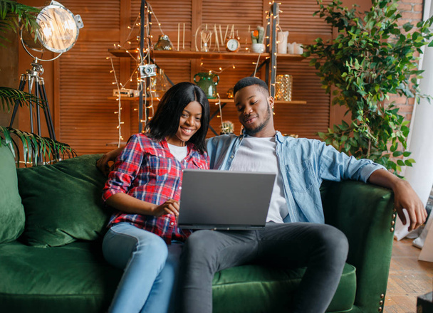 Czarna para siedzi na kanapie i patrząc na laptopa w domu. Szczęśliwy African miłość para leisures w ich dom - Zdjęcie, obraz