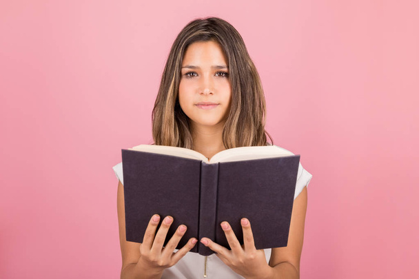Zelfverzekerde jonge vrouw Holding boek over roze achtergrond - Foto, afbeelding