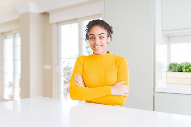 Beautiful african american woman with afro hair wearing a casual yellow sweater happy face smiling with crossed arms looking at the camera. Positive person. - Valokuva, kuva