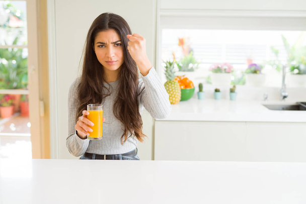 Mladá žena popíjí sklenici čerstvého pomerančového džusu, rozčilená a frustrovaná křikem hněvem, šílenou a křičící s zvedanou rukou, koncept hněvu - Fotografie, Obrázek