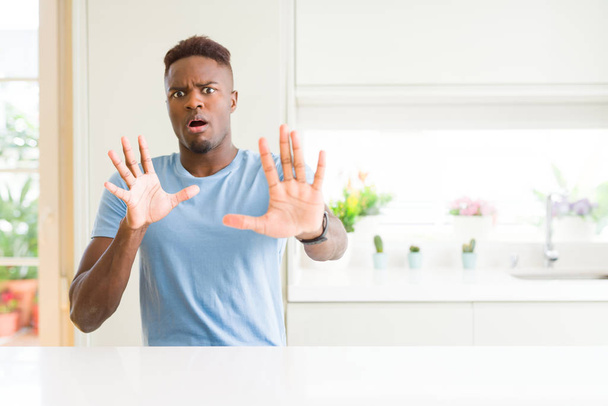 Bell'uomo afroamericano che indossa maglietta casual a casa spaventato e terrorizzato dalla paura espressione fermare il gesto con le mani, gridando sotto shock. Concetto di panico
. - Foto, immagini