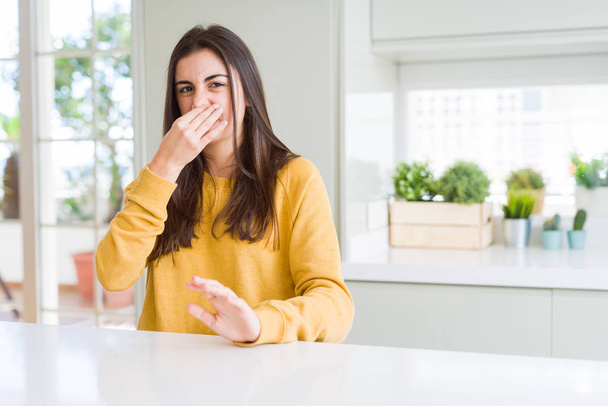 Beautiful young woman wearing yellow sweater smelling something stinky and disgusting, intolerable smell, holding breath with fingers on nose. Bad smells concept. - Photo, Image