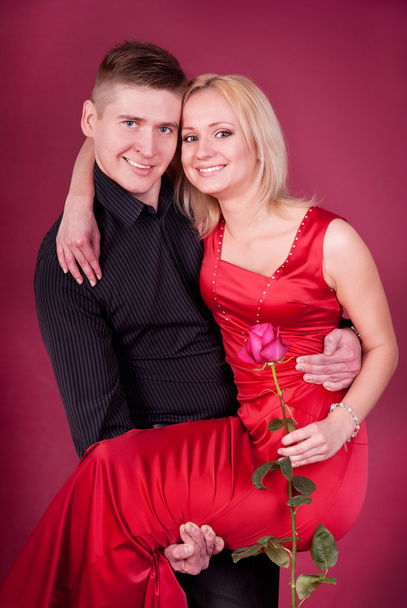 Young couple portrait. Woman in red dress with rose, and man hold her arms - Foto, Bild