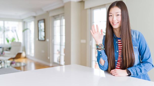 junge schöne asiatische Frau mit langen Haaren trägt Jeansjacke Verzicht auf hallo glücklich und lächelnd, freundliche Willkommensgeste - Foto, Bild