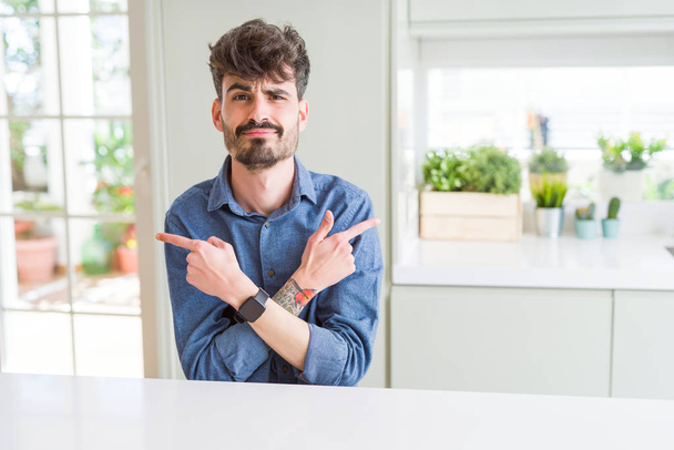 Mladý muž nosí neformální košili sedící na bílém stole ukazování prstem na obě strany, odlišný směr nesouhlasí - Fotografie, Obrázek