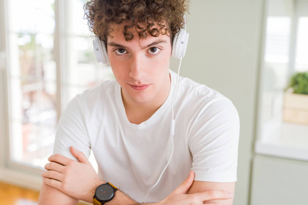 Jongeman die thuis naar muziek luistert met een koptelefoon op zijn hoofd. Ontspannen met een serieuze uitdrukking op zijn gezicht. Eenvoudig en natuurlijk met gekruiste armen - Foto, afbeelding