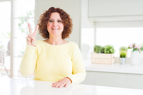 Beautiful senior woman wearing yellow sweater showing and pointing up with fingers number two while smiling confident and happy. - Photo, Image