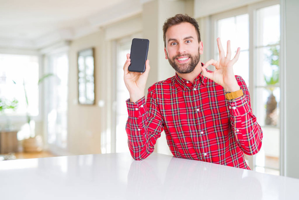 Pohledný muž ukazující na obrazovku smartphone s prsty, výborný symbol - Fotografie, Obrázek
