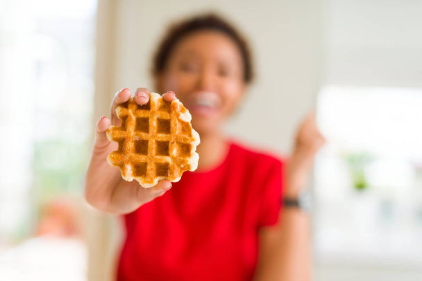 Joven afroamericana americana comiendo dulce waffle gritando orgullosa y celebrando victoria y éxito muy emocionada, animando emoción
 - Foto, Imagen