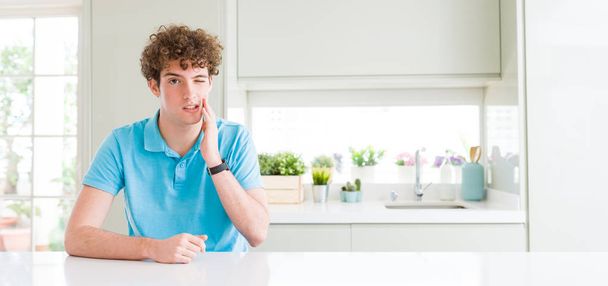 Wide shot of young handsome man at home touching mouth with hand with painful expression because of toothache or dental illness on teeth. Dentist concept. - 写真・画像