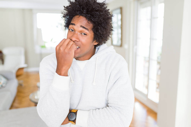 Afrikanisch-amerikanischer Mann mit Sweatshirt, der gestresst und nervös aussieht, die Hände auf den Mund beißenden Nägeln. Angstproblem. - Foto, Bild