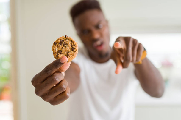 Wiórki czekoladowe młody człowiek african american jedzenia ciasteczka wskazując palcem do aparatu i do Ciebie, ręcznie zarejestrować, gest pozytywny i pewnie z przodu - Zdjęcie, obraz