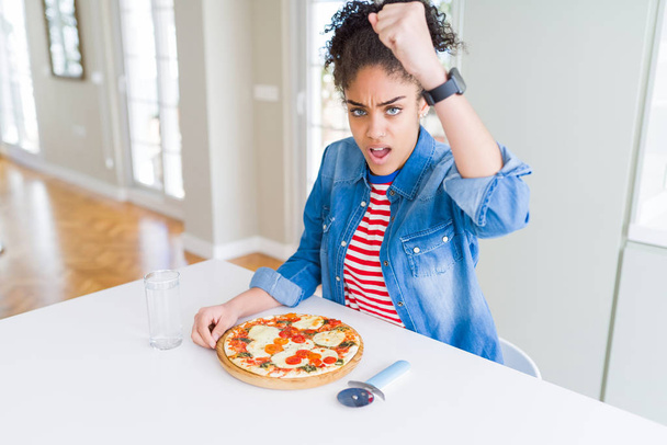 Young african american woman eating homemade mozzarella cheese pizza annoyed and frustrated shouting with anger, crazy and yelling with raised hand, anger concept - Fotoğraf, Görsel