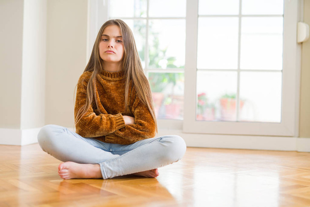 Beautiful young girl kid sitting on the floor at home skeptic and nervous, disapproving expression on face with crossed arms. Negative person. - Photo, Image