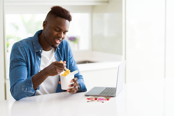 Bello giovane africano business man mangiare consegna asiatico cibo e lavoro utilizzando computer concentrato
 - Foto, immagini
