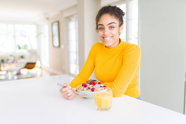 Genç Afrikalı Amerikalı kız mutlu bir yüz ayakta ve kendine güvenen bir gülümseme dişleri gösteren ile gülümseyen kahvaltı için sağlıklı tahıl yeme - Fotoğraf, Görsel