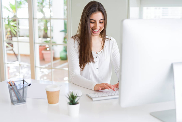 Mooie jonge zakelijke vrouw werken met behulp van computer, glimlachen en geconcentreerd op online werk - Foto, afbeelding