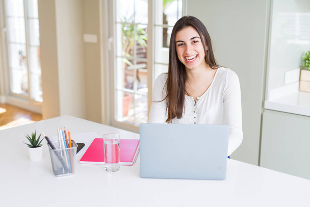 Νεαρή όμορφη γυναίκα χαμογελά ευτυχισμένη και εργάζονται χρησιμοποιώντας φορητό υπολογιστή - Φωτογραφία, εικόνα