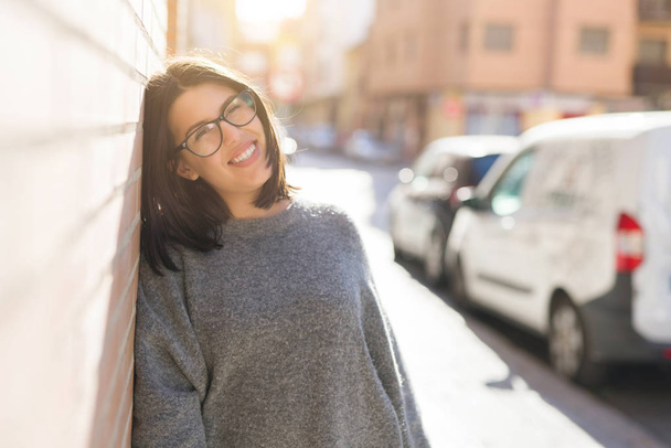 Beautiful young woman wearing glasses smiling cheerful leaning on bricks wall, casual pretty girl at the town - Photo, Image