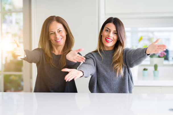 Beautiful family of mother and daughter together at home looking at the camera smiling with open arms for hug. Cheerful expression embracing happiness. - Photo, Image