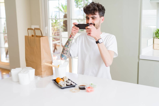 Молодий чоловік фотографує зі смартфоном суші азіатської їжі з доставки
 - Фото, зображення