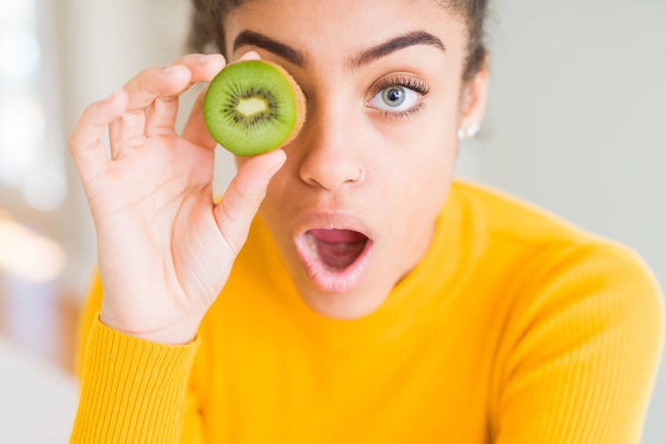 Jovem afro-americana comendo quivi verde assustado em choque com um rosto surpresa, com medo e animado com expressão de medo
 - Foto, Imagem