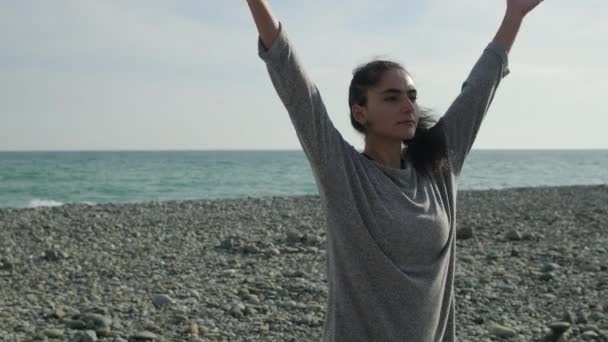 Νεαρή γυναίκα μεσολαβεί στην παραλία της θάλασσας, στέκεται και κουνάει τα χέρια - Πλάνα, βίντεο