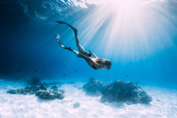 Woman freediver glides with fins. over sandy sea. Freediving and beautiful light in blue ocean - Photo, Image