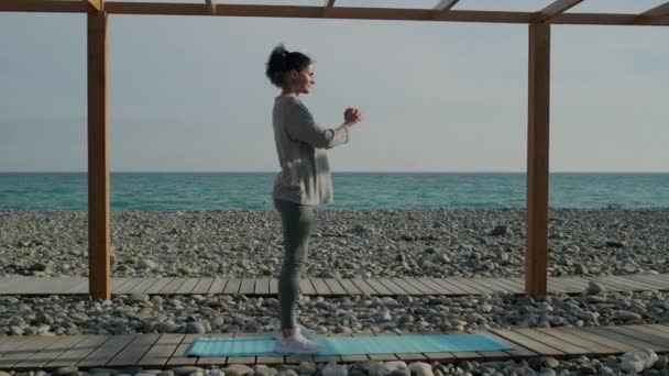 Брюнетка тренирует мышцы ног и ягодиц, приседая на берегу моря
 - Кадры, видео