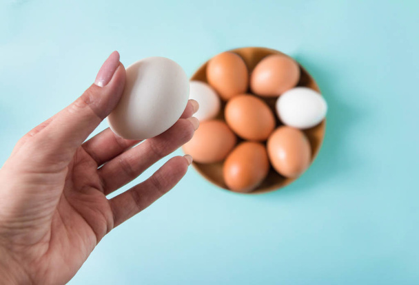 A női keze tart fehér tojást egy fából készült lemez tojással a kék háttér Happy Húsvét. Szelektív fókusz.  - Fotó, kép