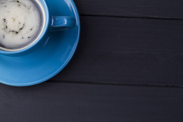Café en taza azul con plato que le hace juego en fondo de madera negra en una esquina con espacio negativo para texto
 - Foto, Imagen