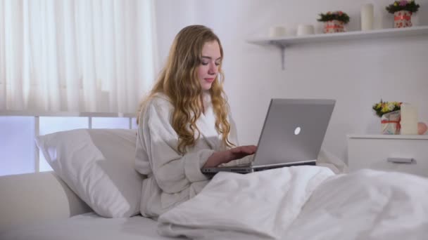 Cute girl working on laptop from early morning, dressed in bathrobe, freelance - Imágenes, Vídeo
