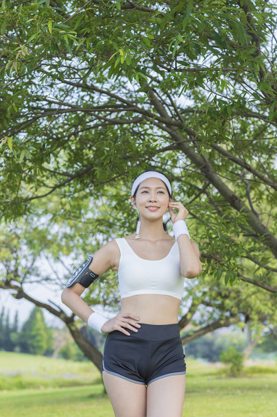 Beautiful young asian woman doing sport in headphones  in park - Фото, зображення