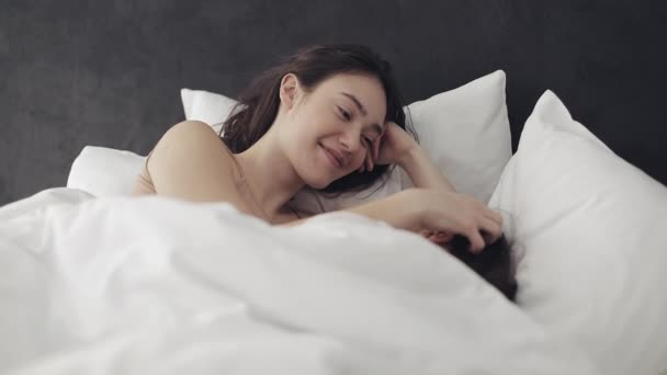 Lesbian couple hugging and smiling while lying together in bed at home. Young lesbians kisses and hugs after wake up - Filmati, video