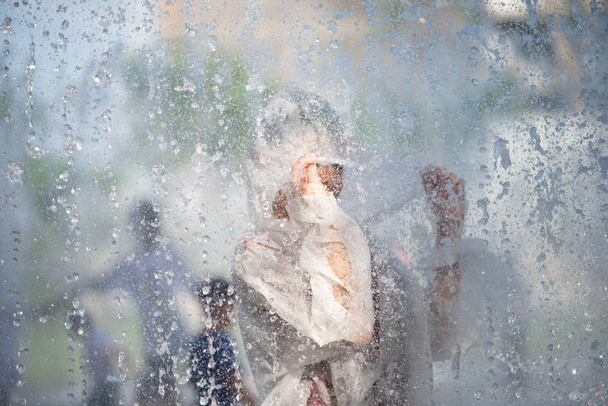 Menino jogando água gotas fonte sob o pano e guarda-chuva
 - Foto, Imagem