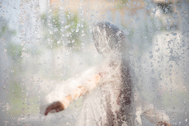 Menino jogando água gotas fonte sob o pano e guarda-chuva
 - Foto, Imagem