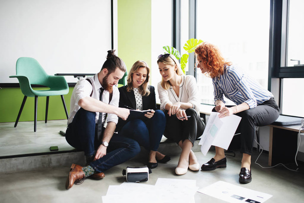 A group of young business people sitting on the floor in an office, talking. - Fotoğraf, Görsel