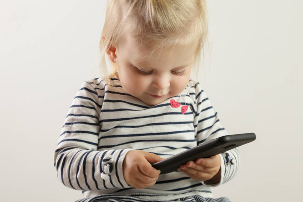 Στούντιο πορτρέτο του ένα χαριτωμένο ξανθιά κοριτσάκι κρατώντας ένα κινητό τηλέφωνο - Φωτογραφία, εικόνα