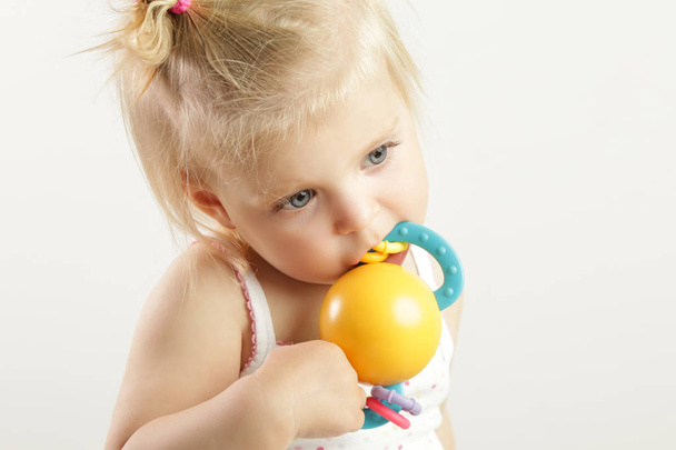 Очаровательная малышка жует режущую игрушку, чтобы облегчить боль в деснах.
. - Фото, изображение
